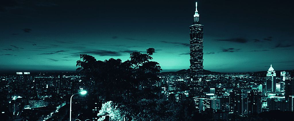 Taipei 101 and the Xinyi District skyline at night, seen against a dark sky.
